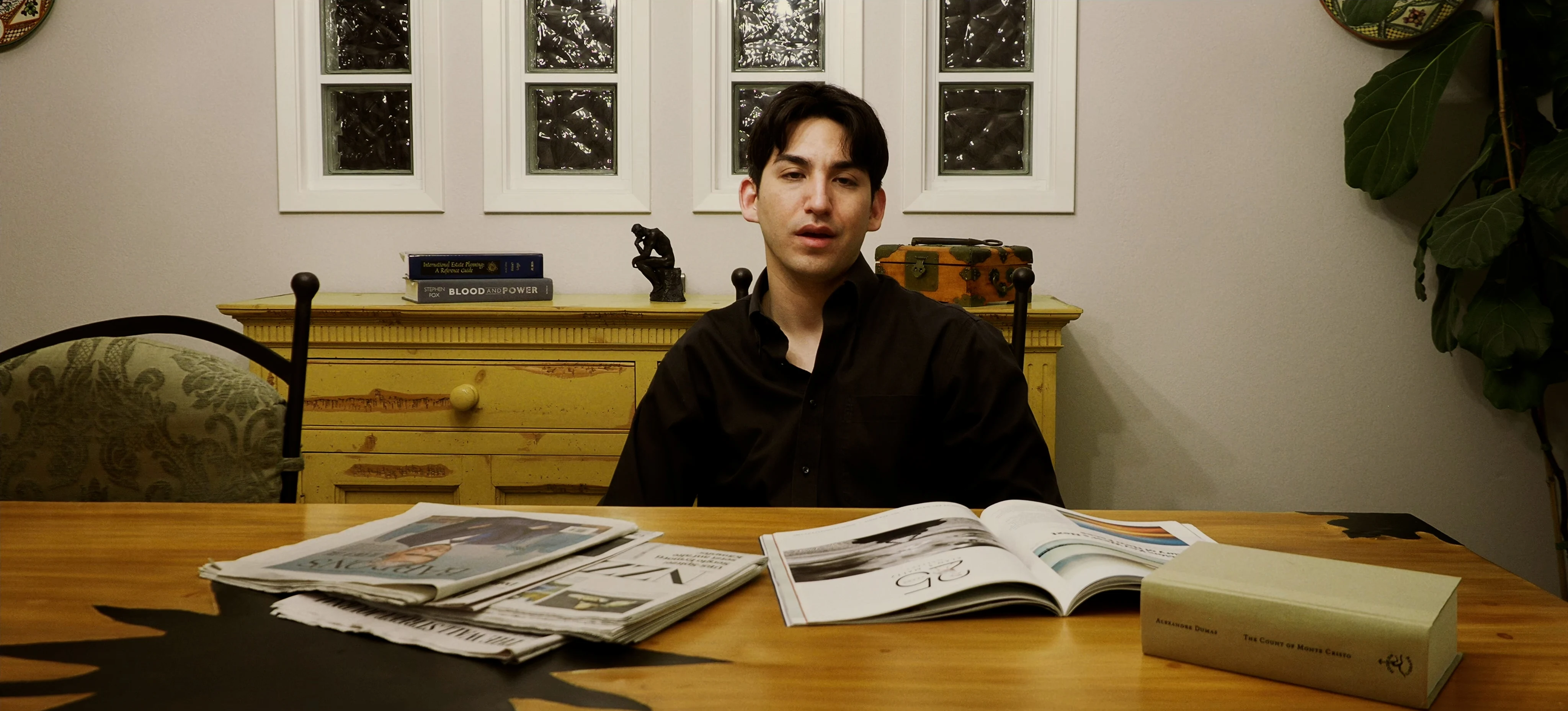 Ian Bloom as The Suit in Star Vehicle speaking in a dark room in formal attire