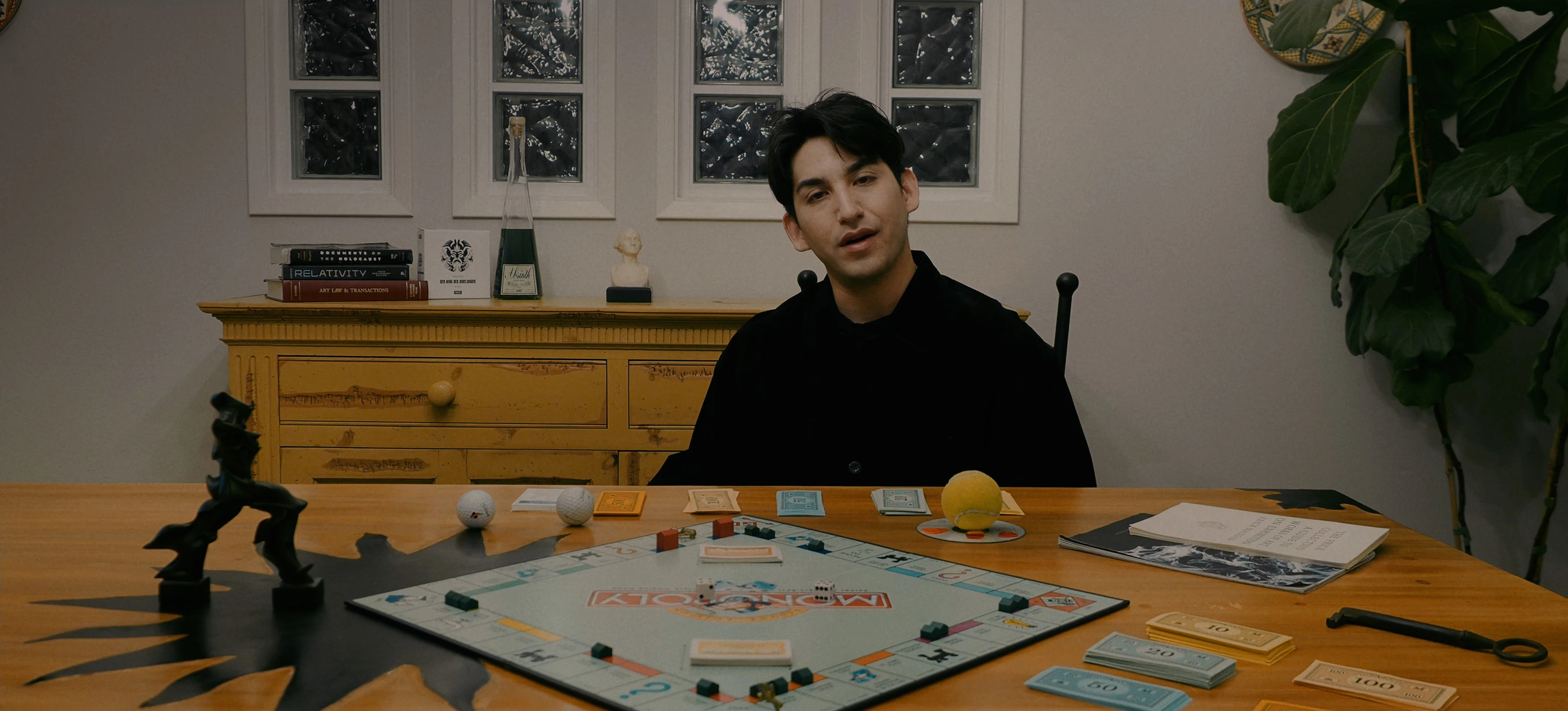 Ian Bloom as The Suit in Star Vehicle seated in profile in a shadowed interior